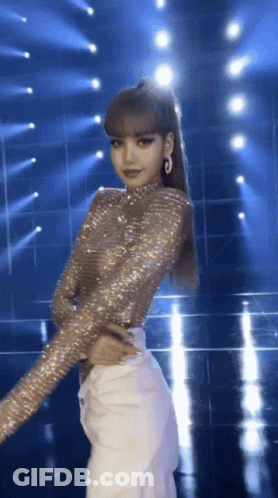 A Woman In A Sequined Top And White Pants Stands On A Stage GIF