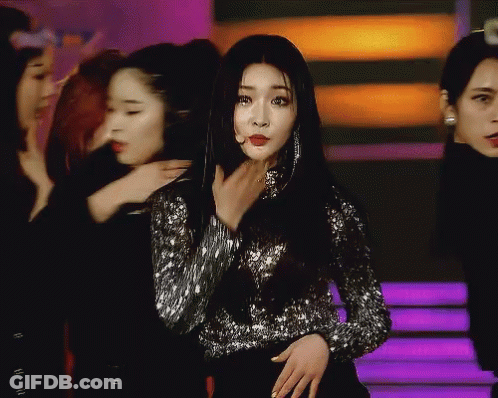 A Woman In A Sequined Top Stands In Front Of A Group Of Girls GIF