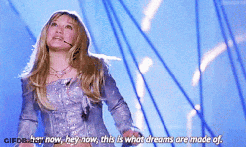 A Woman In A Silver Dress Is Standing On A Stage And Saying Hey Now Hey Now This Is What Dreams Are Made Of GIF