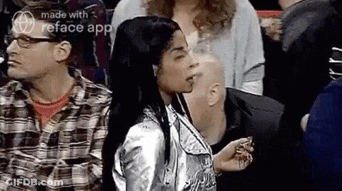 A Woman In A Silver Jacket Is Standing In A Crowd Of People And Smoking A Cigarette . GIF