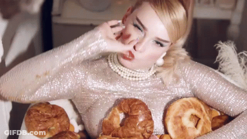 A Woman In A Silver Sequined Dress Is Holding A Tray Of Bread GIF