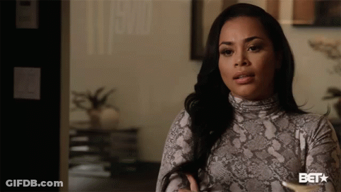 A Woman In A Snake Print Turtleneck Sweater Is Standing In Front Of A Bet Sign GIF