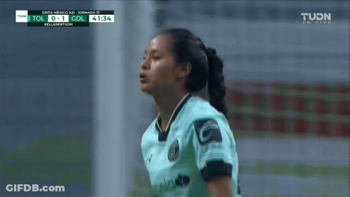 A Woman In A Soccer Uniform Stands In Front Of A Tv Screen That Says Tudn On It GIF