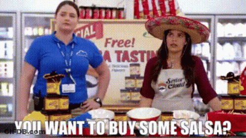 A Woman In A Sombrero Is Standing Next To Another Woman In An Apron In A Store . GIF