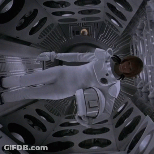 A Woman In A Space Suit Is Holding A Helmet With The Letter O On It GIF