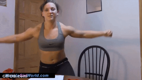 A Woman In A Sports Bra Is Standing In Front Of A Chair With The Website Musclegirlworld.com Written On The Bottom GIF