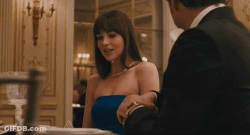 A Woman In A Strapless Blue Dress Is Sitting At A Table With A Man In A Suit GIF