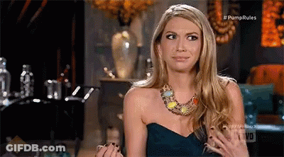 A Woman In A Strapless Dress And Necklace Is Sitting On A Couch . GIF