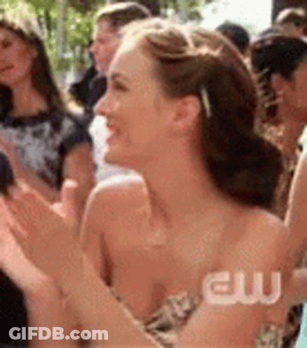 A Woman In A Strapless Dress Is Clapping In A Crowd Of People . GIF