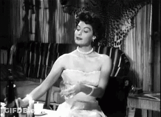 A Woman In A Strapless Dress Is Sitting At A Table With A Candle . GIF