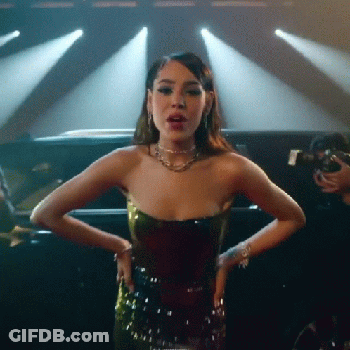 A Woman In A Strapless Dress Is Standing In Front Of A Car On A Stage . GIF