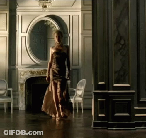 A Woman In A Strapless Dress Walks Through A Room GIF