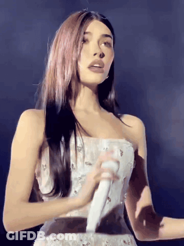 A Woman In A Strapless White Dress Is Holding A Microphone GIF