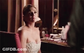 A Woman In A Strapless White Dress Is Sitting In Front Of A Mirror . GIF