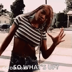 A Woman In A Striped Crop Top And Shorts Is Standing On A Sidewalk And Saying So What 'S Up ? GIF