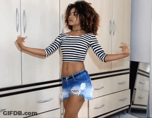 A Woman In A Striped Crop Top And Shorts Stands In Front Of A Dresser GIF
