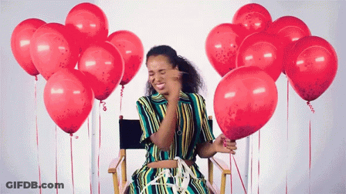 A Woman In A Striped Dress Is Sitting In A Chair With Red Balloons Around Her GIF