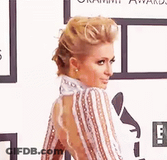 A Woman In A Striped Dress Is Standing On A Red Carpet At An Event . GIF
