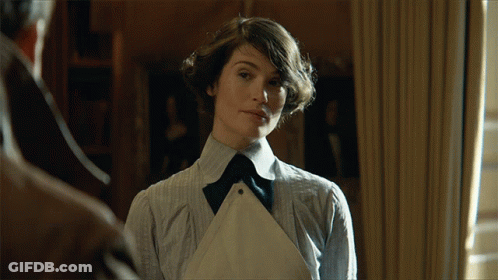 A Woman In A Striped Shirt And Apron Stands In Front Of A Window GIF