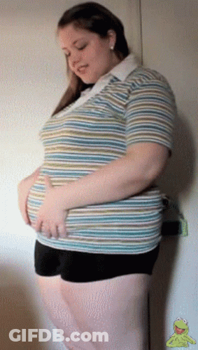 A Woman In A Striped Shirt And Black Shorts Holds Her Stomach GIF