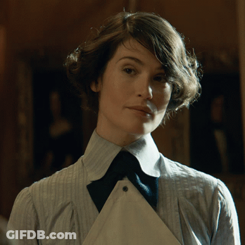 A Woman In A Striped Shirt And Tie Looks At The Camera GIF