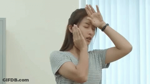 A Woman In A Striped Shirt Is Covering Her Face With Her Hands While Standing In Front Of A Window . GIF