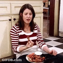 A Woman In A Striped Shirt Is Eating Chicken Wings In A Kitchen . GIF