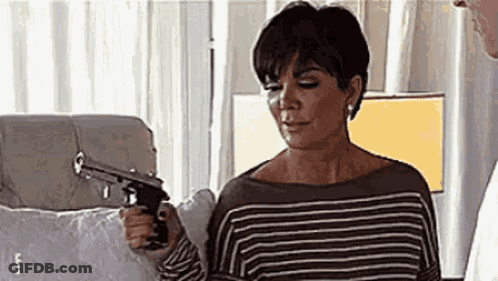 A Woman In A Striped Shirt Is Holding A Gun . GIF