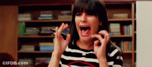 A Woman In A Striped Shirt Is Screaming And Holding A Cell Phone In Her Hand . GIF