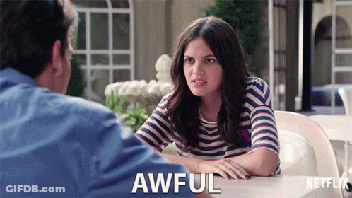 A Woman In A Striped Shirt Is Sitting At A Table With A Man And Says Awful In Front Of Her GIF