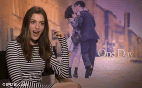 A Woman In A Striped Shirt Is Sitting In Front Of A Picture Of A Man And Woman Kissing With The Words One Day Above Them GIF