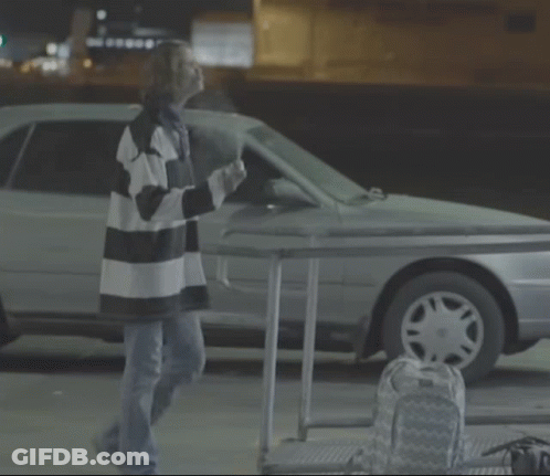 A Woman In A Striped Shirt Is Standing In Front Of A Car GIF