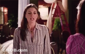 A Woman In A Striped Shirt Is Talking To Another Woman In A Living Room . GIF