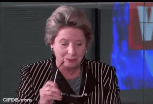 A Woman In A Striped Suit Holds A Pair Of Glasses In Her Hand GIF
