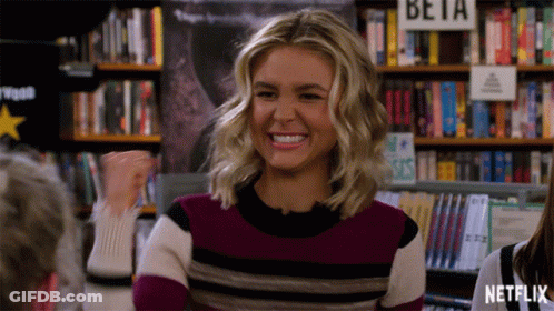 Woman In Striped Sweater Smiling In Front Of Beta Sign GIF