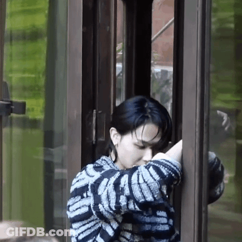 A Woman In A Striped Sweater Is Standing In Front Of A Glass Door . GIF