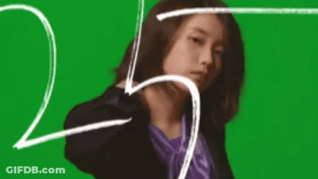 A Woman In A Suit And A Purple Shirt Is Standing In Front Of A Green Screen . GIF