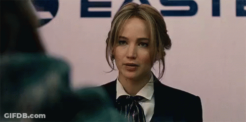A Woman In A Suit And Bow Tie Is Standing In Front Of A Sign . GIF