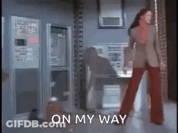 A Woman In A Suit And Red Pants Is Standing In A Room With The Words On My Way Written On The Floor . GIF