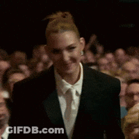 A Woman In A Suit And Tie Is Clapping In Front Of A Crowd . GIF