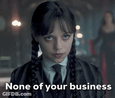A Woman In A Suit And Tie Is Looking At The Camera With The Words `` None Of Your Business '' Written Below Her . GIF
