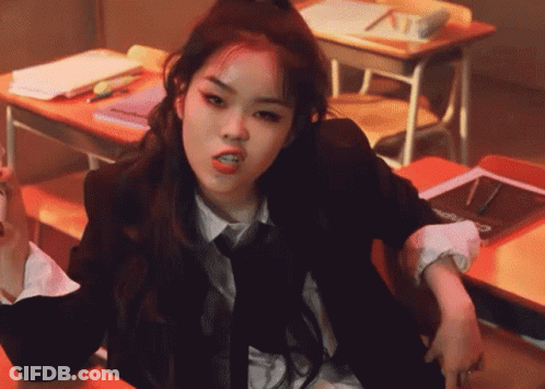 A Woman In A Suit And Tie Is Sitting At A Desk GIF