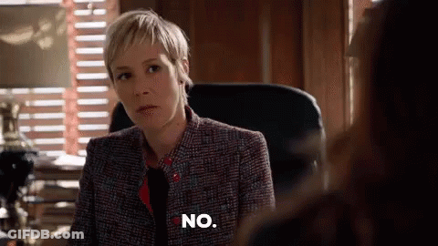 A Woman In A Suit And Tie Is Sitting In A Chair And Says No . GIF