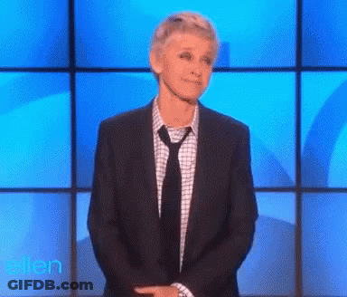 A Woman In A Suit And Tie Is Standing In Front Of A Blue Wall With The Word Ellen On It GIF