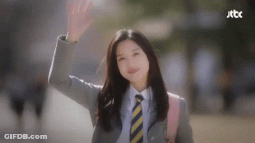 A Woman In A Suit And Tie Is Waving Her Hand . GIF
