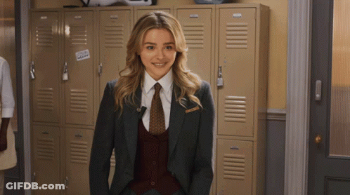 A Woman In A Suit And Tie Stands In Front Of A Row Of Lockers With A Sticker That Says Cold GIF