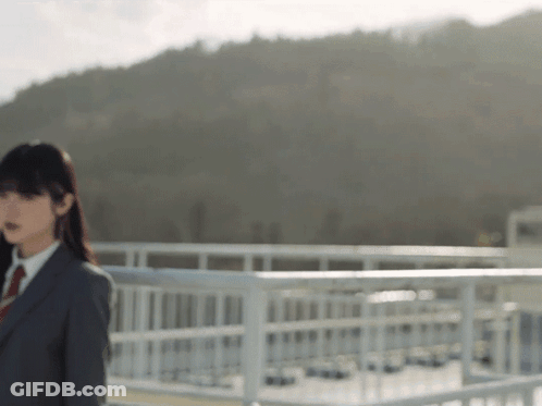 A Woman In A Suit And Tie Stands On A Bridge GIF