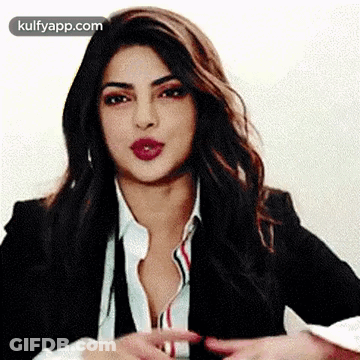 A Woman In A Suit And White Shirt Is Making A Gesture With Her Hands . GIF