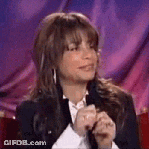A Woman In A Suit And White Shirt Is Sitting In Front Of A Purple Curtain . GIF