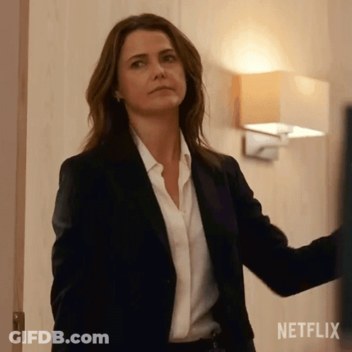 A Woman In A Suit And White Shirt Is Standing In A Room . GIF